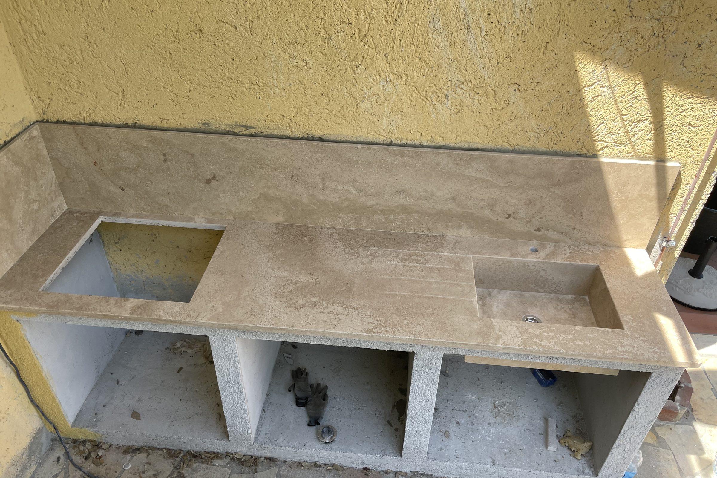 Piano per cucina esterna in travertino con lavello e alzata, in fase di posa
