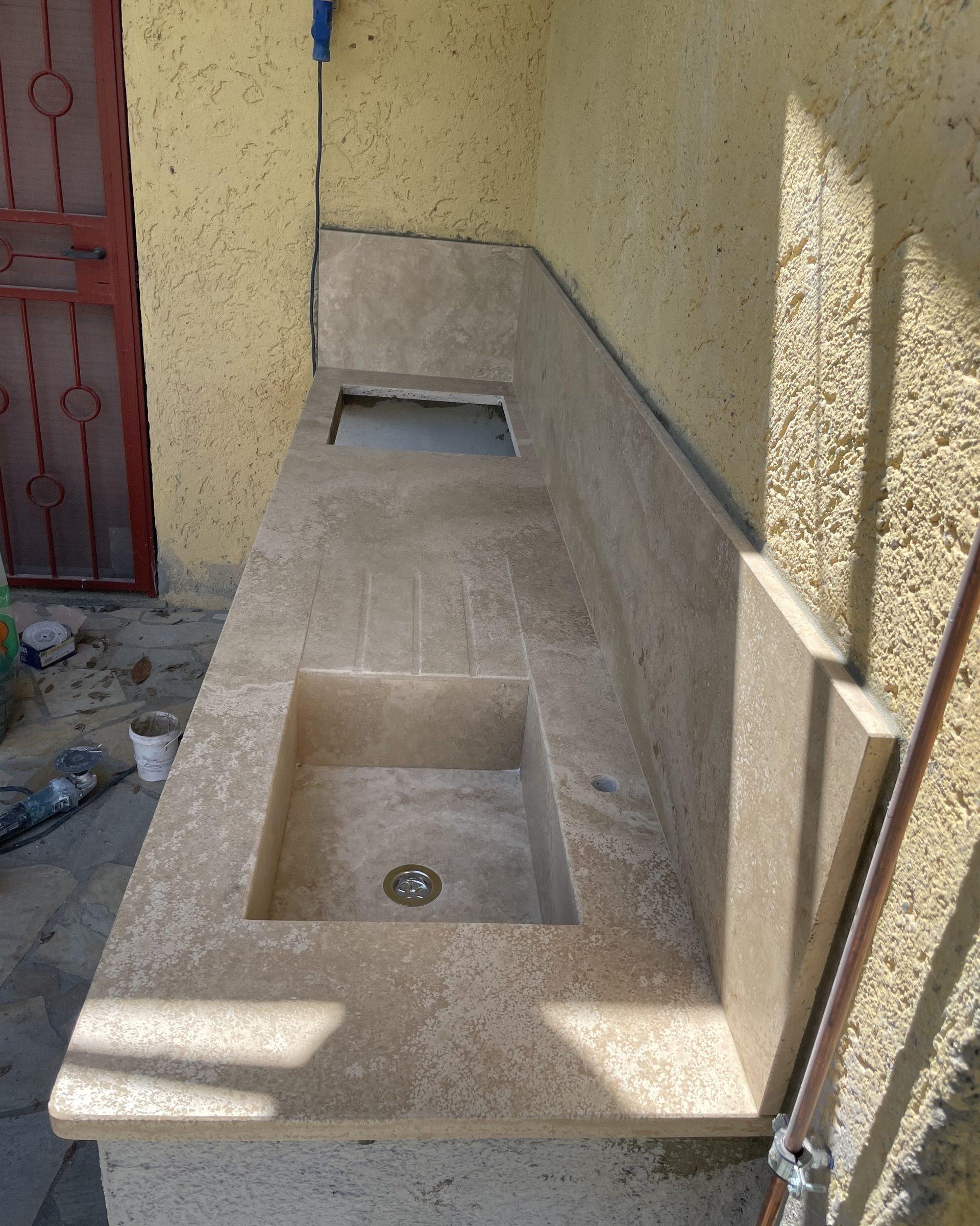 Lavatoio esterno in travertino con piano di servizio, in fase di posa