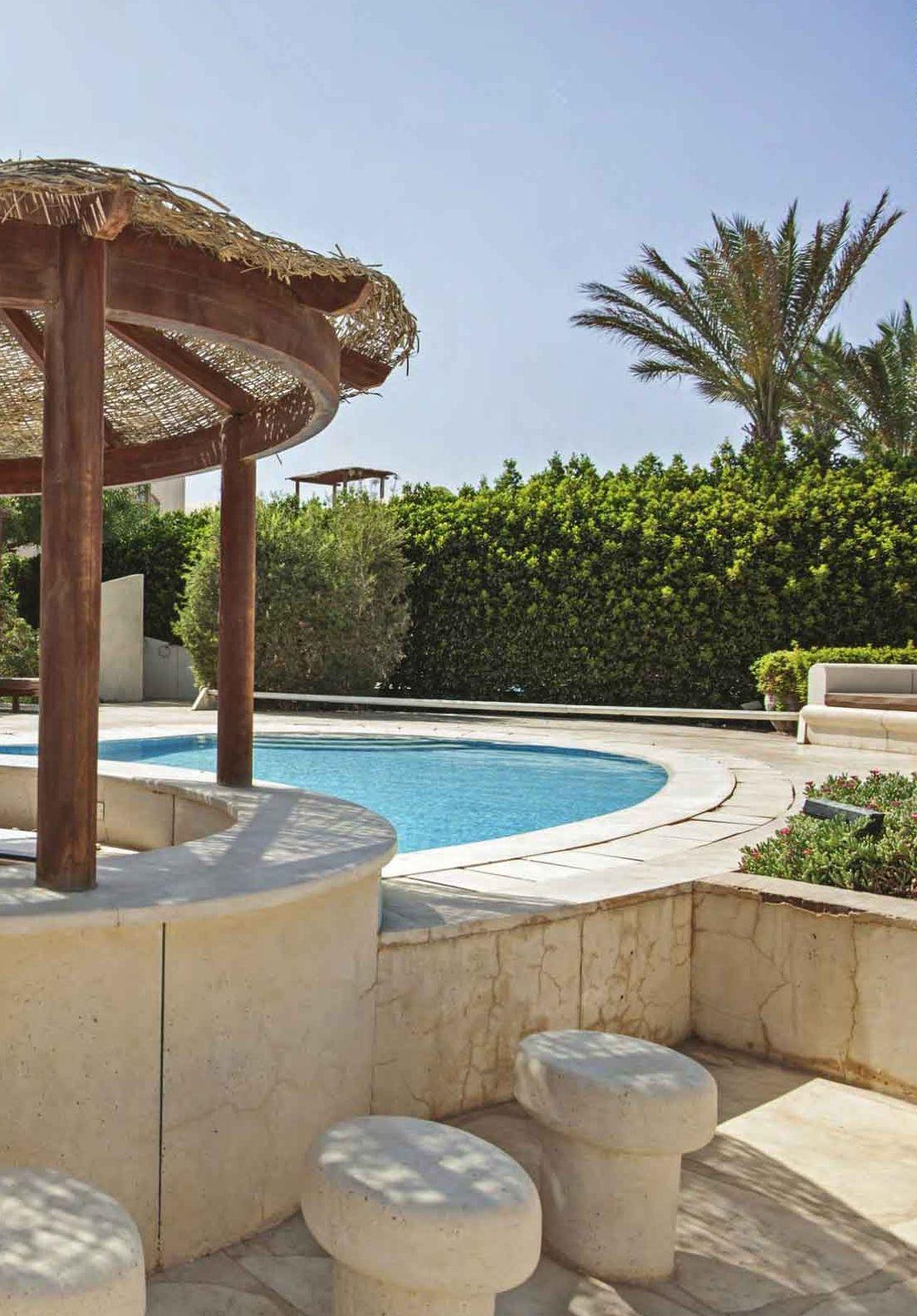 Bordo piscina curvo in pietra con sedute e pergola