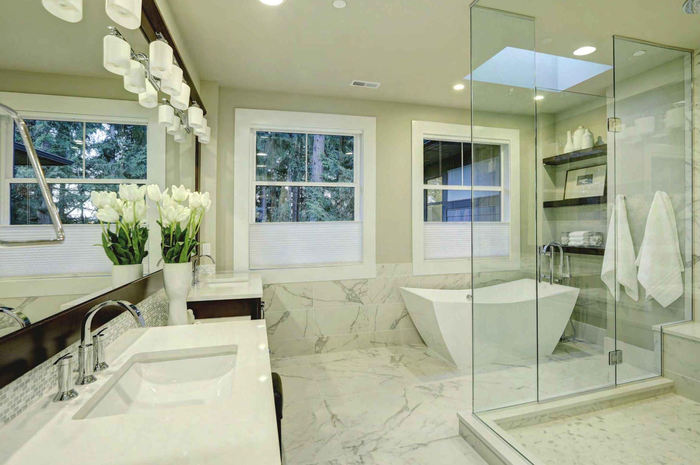 Bagno rivestito in marmo bianco con vasca freestanding e doccia in vetro
