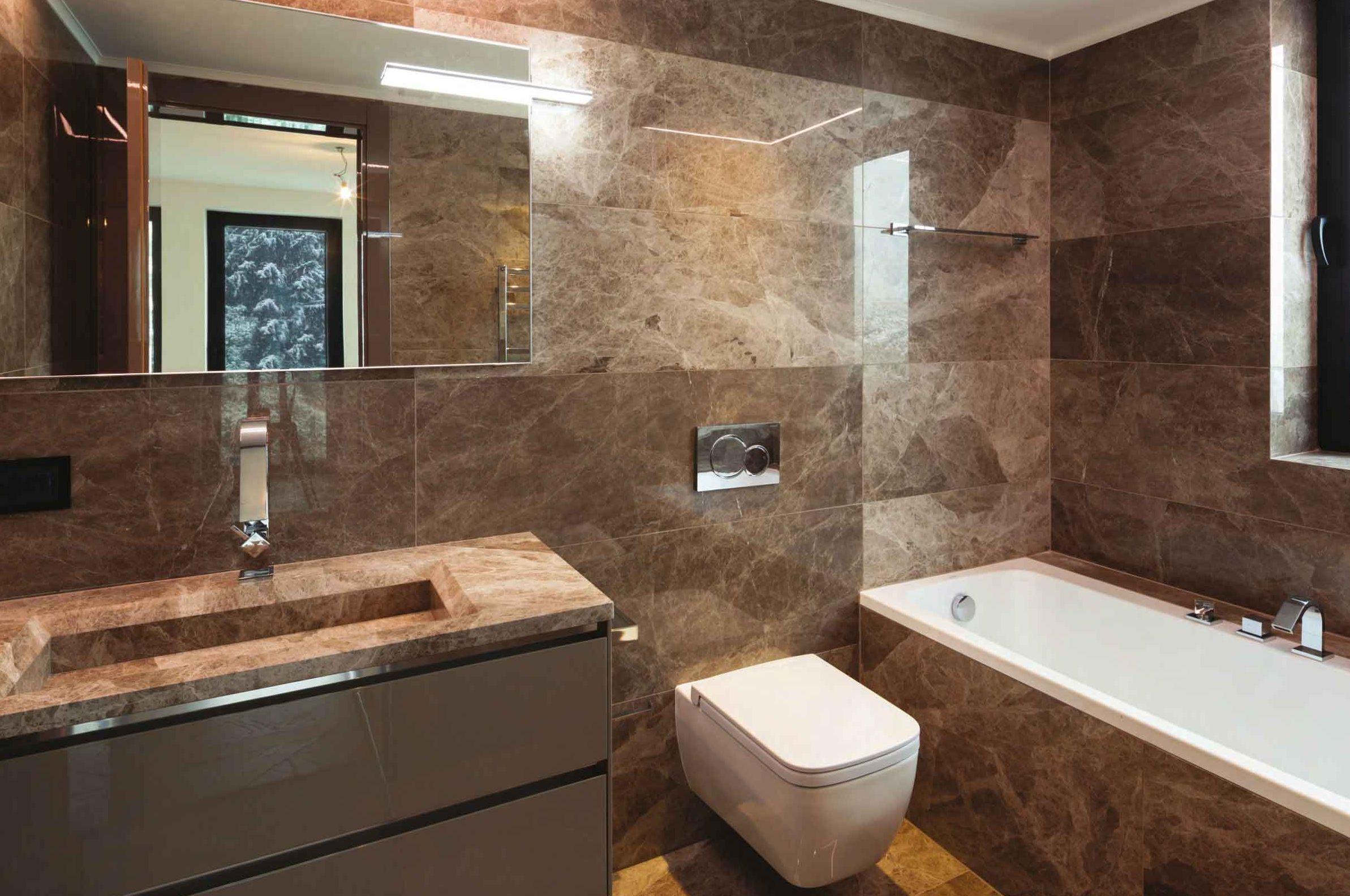 Bagno rivestito in marmo bruno con lavabo scavato nel piano e vasca
